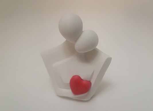 White clay figures of a couple hugging with a red heart on a light beige background