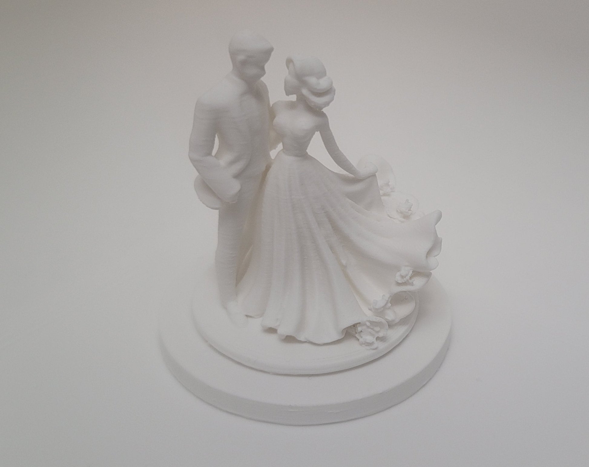 White wedding cake topper with a couple on a plain white background