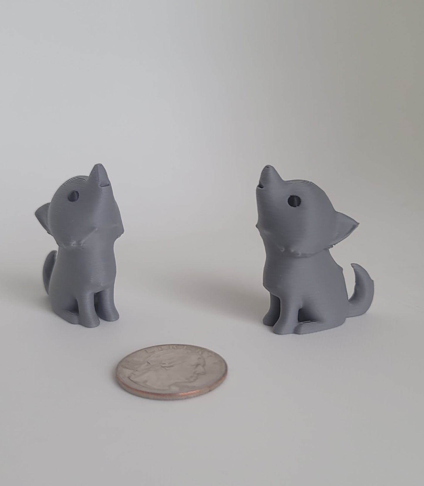 Gray 3D printed dire wolf keychain and desk toy, two wolves facing each other with quarter for scale, made in Reno NV