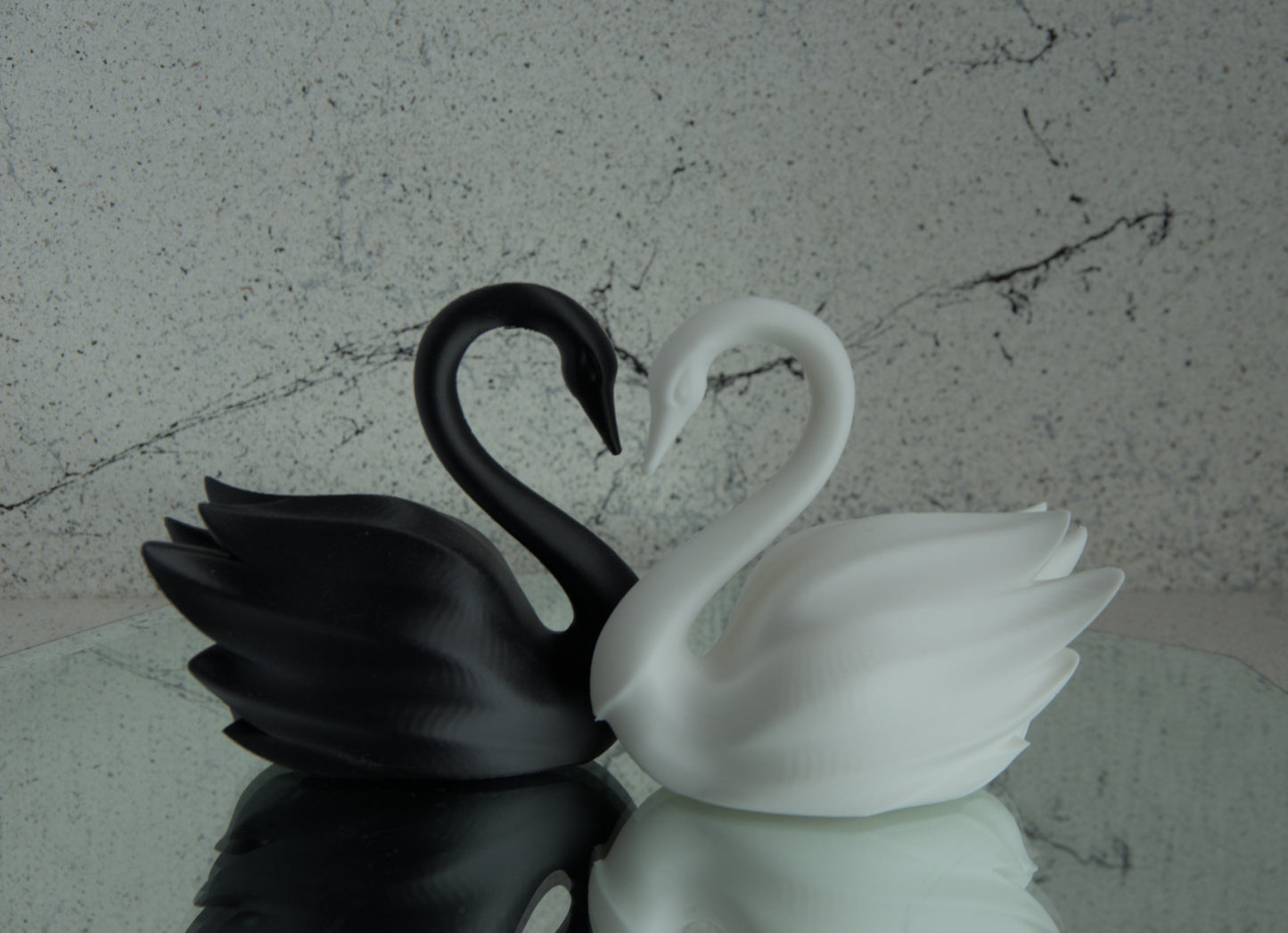 Black and white swan figurines on a reflective surface with a textured gray background