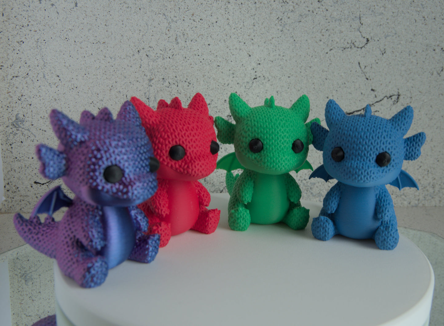 Four colorful dragon-shaped toys on a white surface with a gray textured background