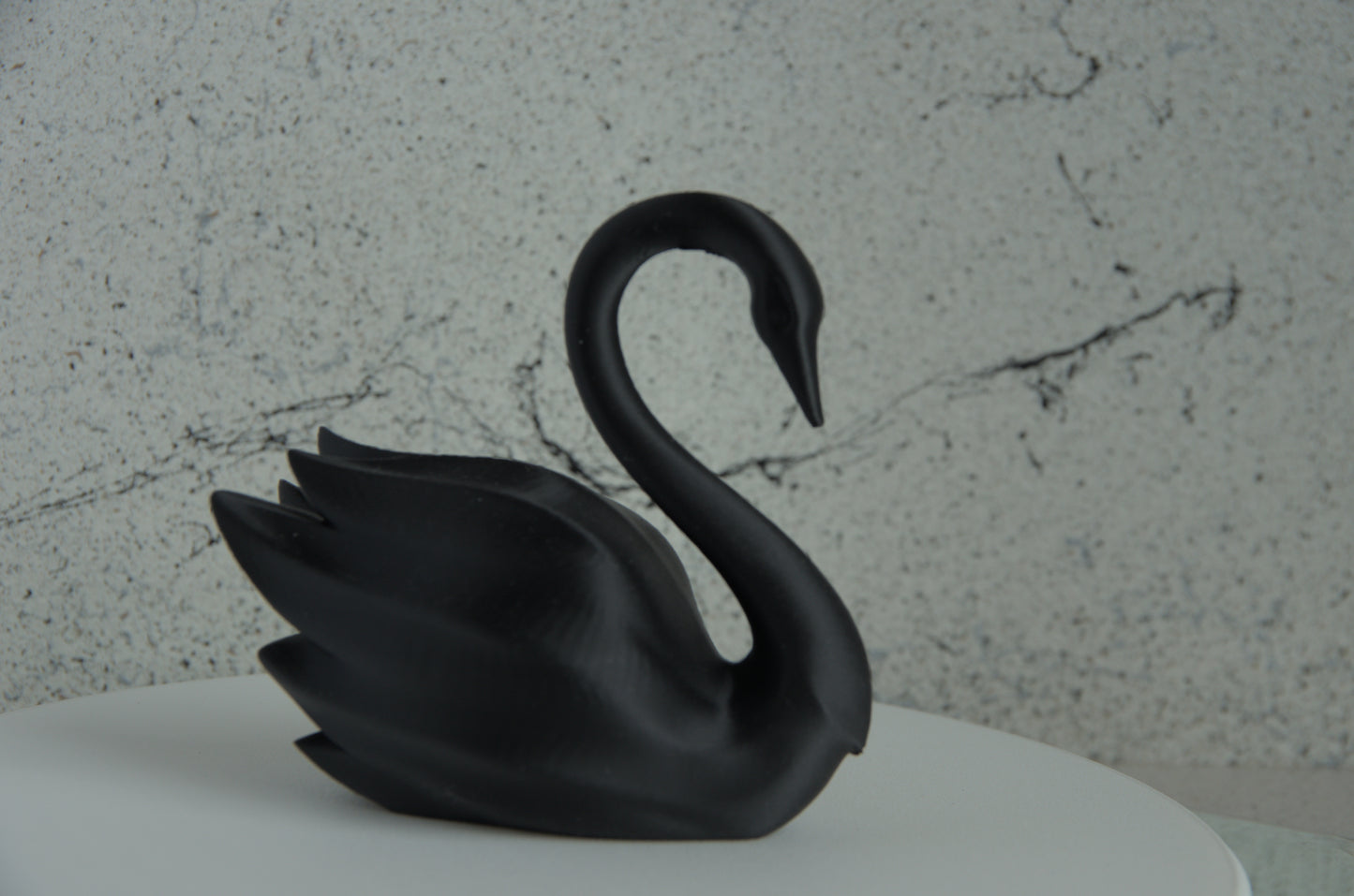 Black 3D printed swan figurine on a white surface with marble-textured background