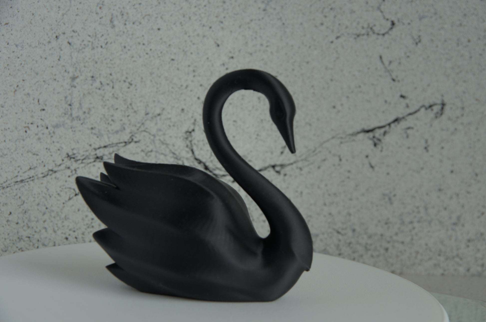 Black 3D printed swan figurine on a white surface with marble-textured background