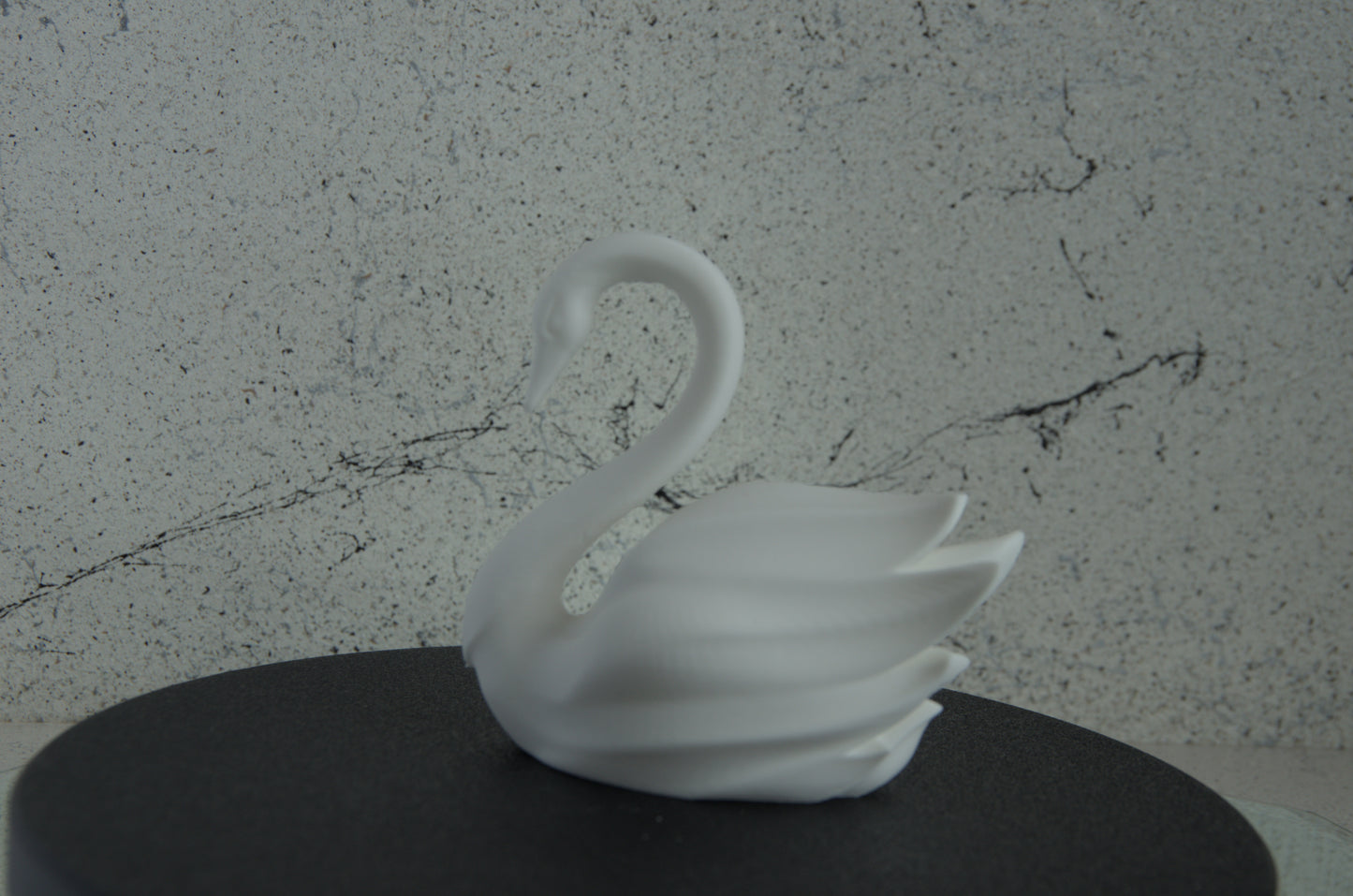 White 3D printed swan figurine on a dark surface with marble-textured background