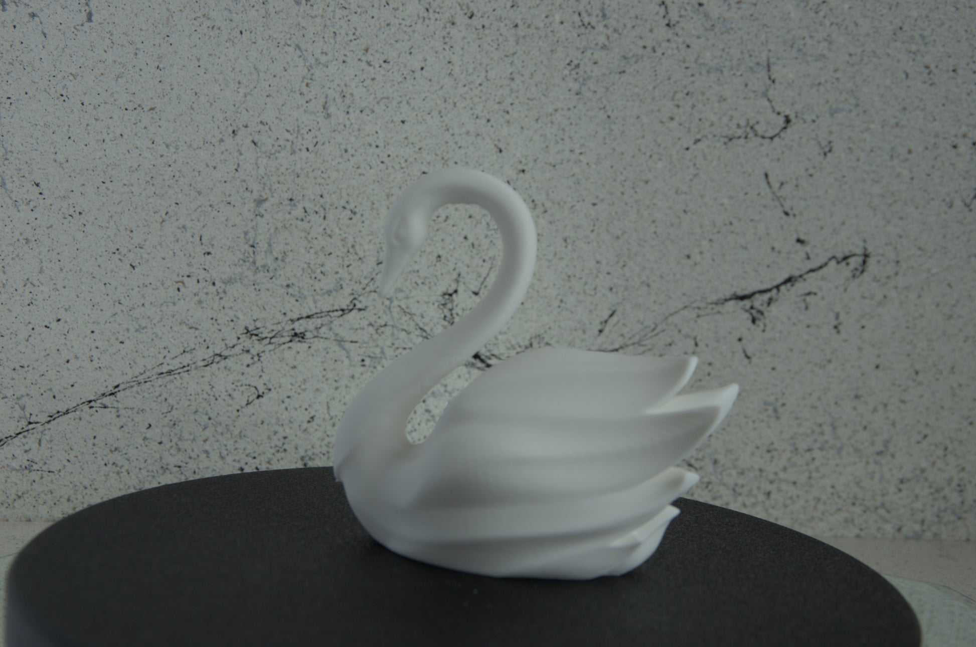 White 3D printed swan figurine on a dark surface with marble-textured background