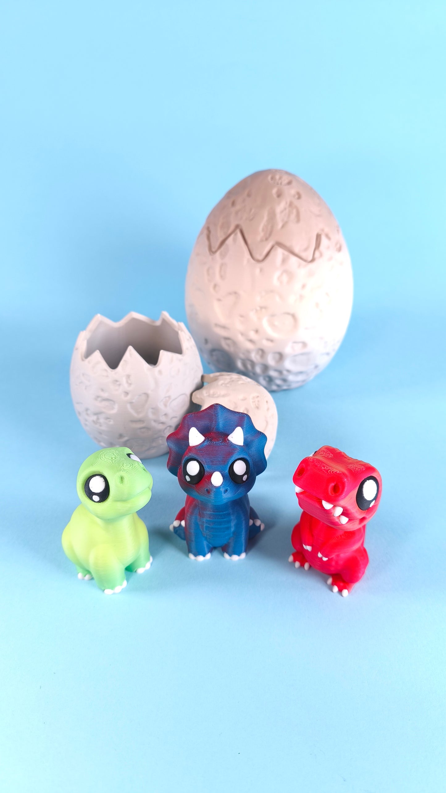 Full 3D printed Finger Dinosaur Pack — green T-rex, blue triceratops, and red T-rex figures with cracked dino egg shells on a light blue background