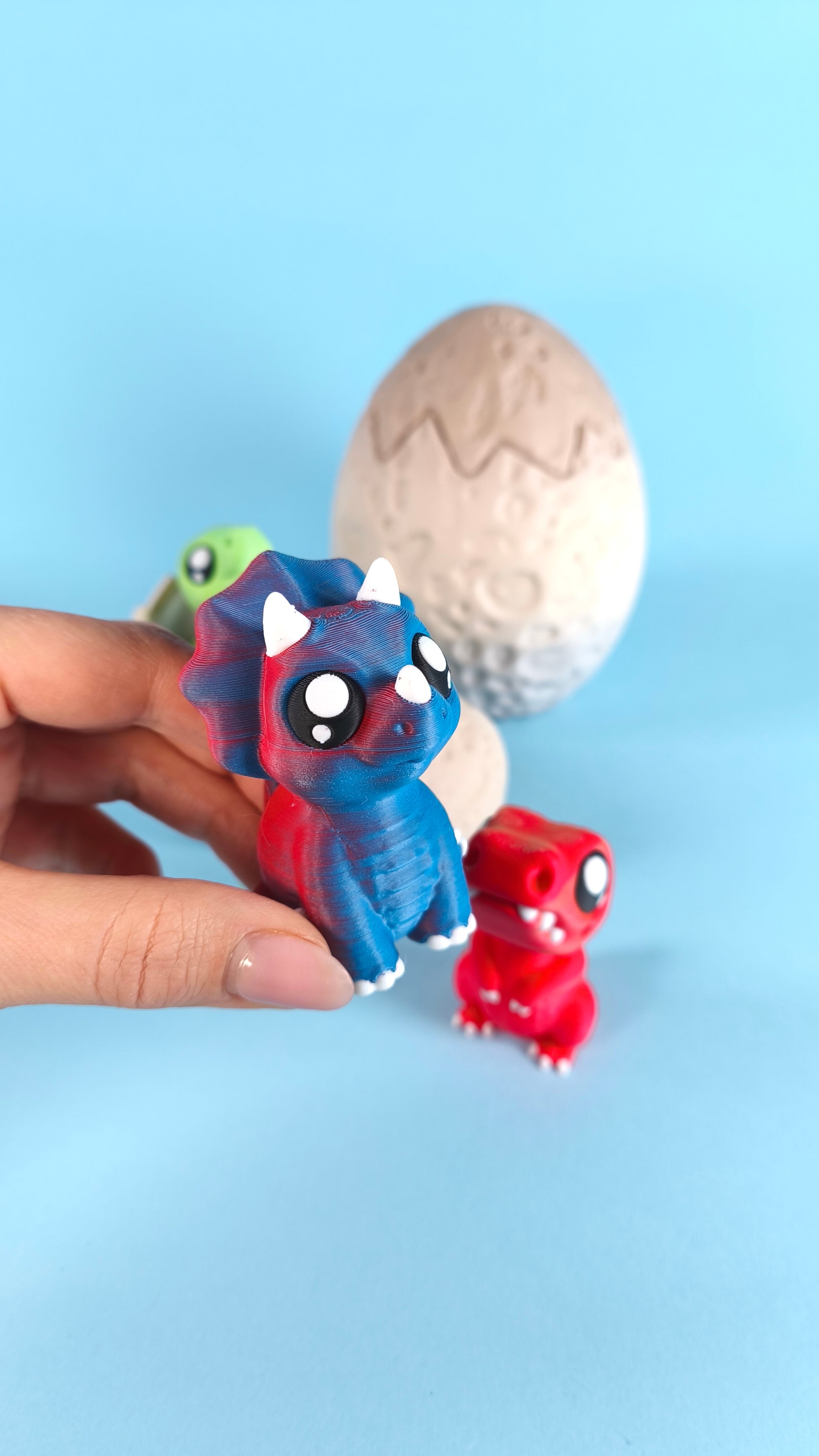 3D printed baby dinosaur finger puppets with hatching dino eggs on a light blue background